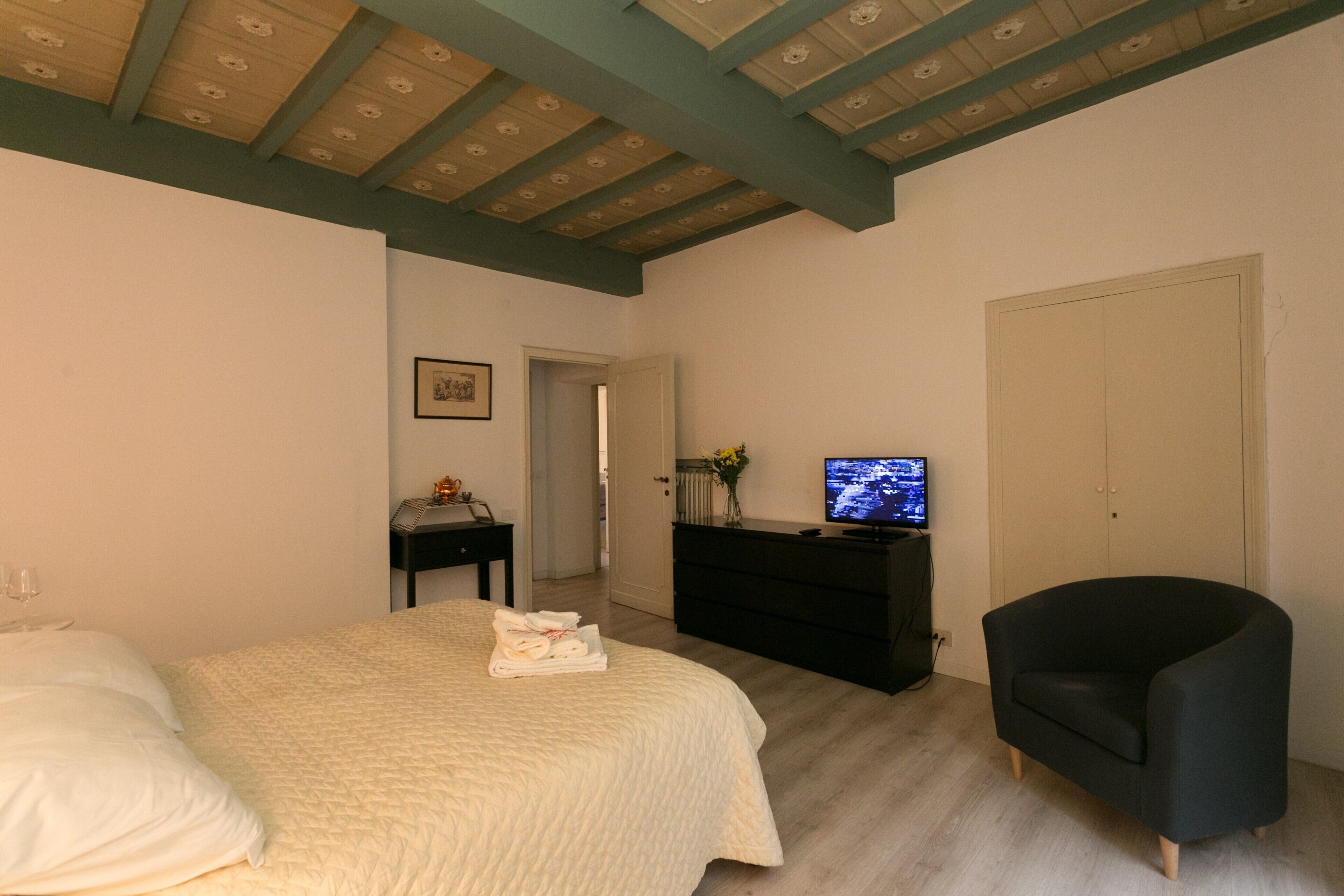 Un dormitorio con una cama, un sillón negro, un televisor y un aparador.