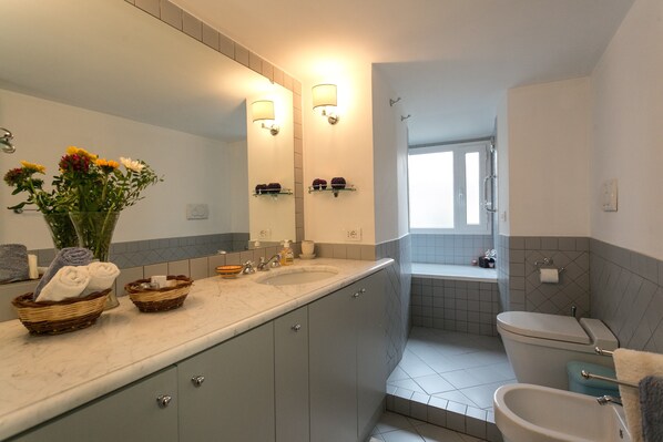 A bathroom with a sink, mirror, and toilet. There are baskets with towels and a vase of flowers on the counter. - Parione House apartment in the center of Rome (Roma)