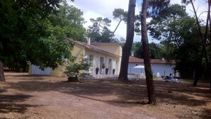 A building with a yellow facade and white shutters, surrounded by trees and a grassy area. - Villa in wooded park 3 bedrooms / sleeps 7 (La Tremblade)