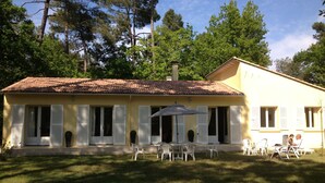A yellow building with a tiled roof, white shutters, and a patio with outdoor furniture. - Villa in wooded park 3 bedrooms / sleeps 7 (La Tremblade)