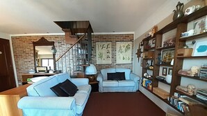 Una sala de estar con pared de ladrillo, una escalera, un sofá azul, una estantería y una mesa de centro.