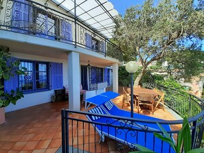 Um edifício de dois andares com área externa coberta, incluindo uma mesa e cadeiras, e uma escadaria que dá acesso ao andar superior.