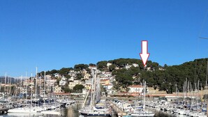 Una marina con numerosos barcos amarrados, una colina con edificios y un cielo azul despejado.
