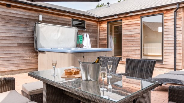 An outdoor patio with wicker furniture, a glass table, a grill, and a hot tub.
