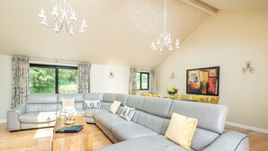 A spacious living room with a large grey sectional sofa, a wooden coffee table, and a chandelier.
