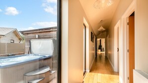 A modern home interior with a wooden floor hallway, a hot tub, and a large window.