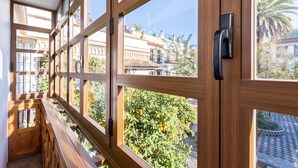 Un balcone in legno con ampie finestre che si affaccia su un giardino e degli edifici.