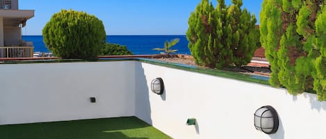 Terrassa al terrat amb vistes al mar, gespa artificial verda i paret blanca amb dues làmpades murals.