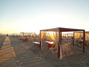 A beach with sunbeds and a covered seating area.