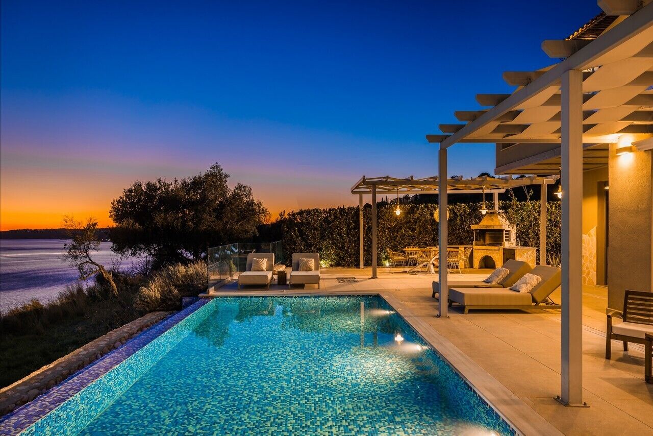Piscina com vista para o pôr do sol, cadeiras de descanso e um pergolado.