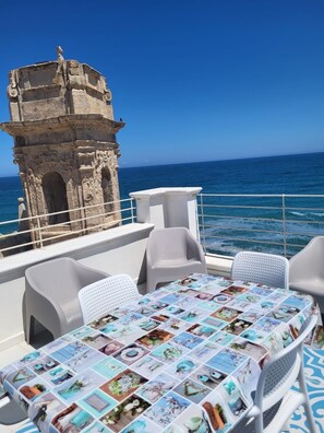 A dining area with a table covered in a collage of images, overlooking the sea with a stone tower in the background. - SAN SALVATORE HOUSE - house in the historic center - spectacular sea view terrace (Monopoli)