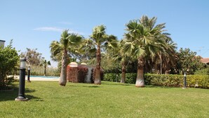 A well-maintained grassy area with palm trees and a small building with a red roof. - Beachside new luxury apartment with sea & mountain views, great location & Wi-FI (Dénia)