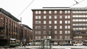 A tram station with a bus stop, a tram, and a building with multiple floors and windows. - 2ndhomes Bright Top Floor Studio in Fredrikinkatu (Helsinki)