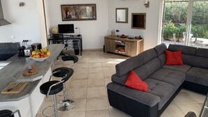 A modern living space with a kitchen area, a dining table, and a grey sectional sofa with red cushions. - Beautiful villa with sea view and Ile Rousse (Monticello)