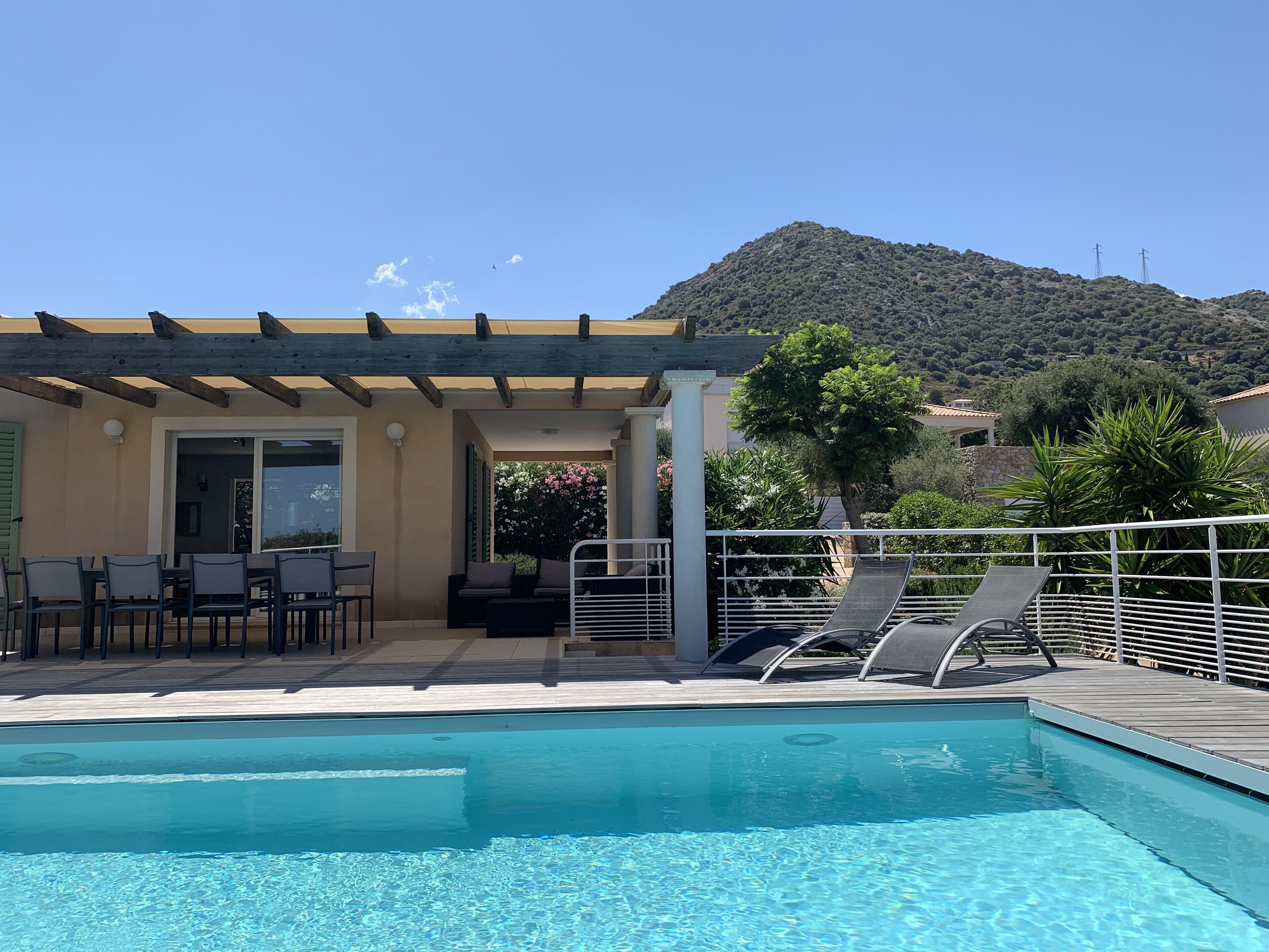 A pool area with lounge chairs, a covered seating area, and a view of a mountain.