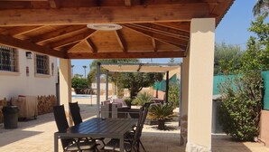 Ein Außenbereich mit Terrasse, einer Holz-Pergola, einem Tisch mit Stühlen und einer Steinsäule.
