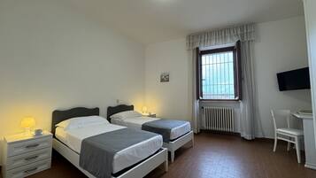 Habitación de hotel con dos camas, un escritorio, una silla, un televisor y una ventana con cortinas.