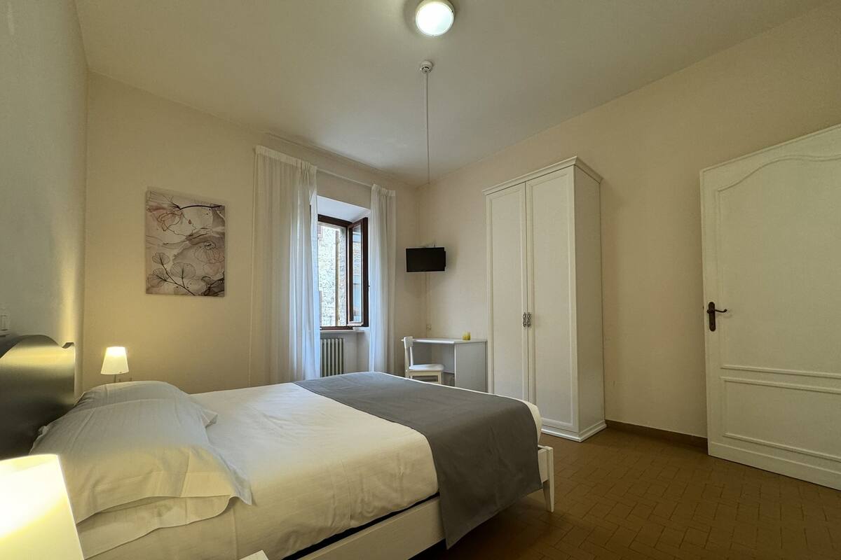 A bedroom with a bed, bedside table, lamp, wardrobe, and a window with curtains.