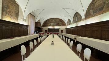 Een lange tafel met witte stoelen in een ruimte met gewelfde plafonds en fresco's op de muren.