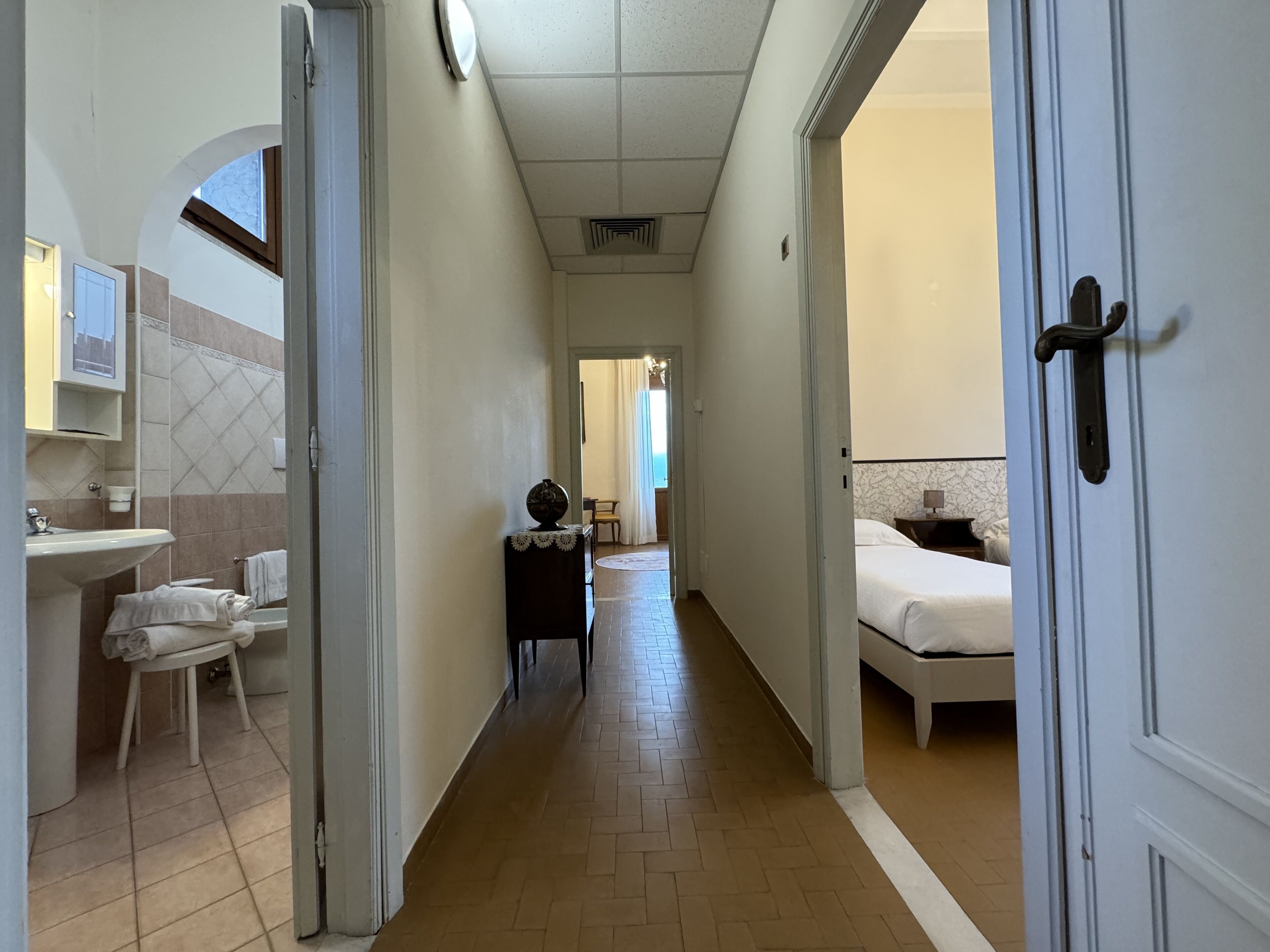 A hotel corridor with a bathroom on the left, a dining area in the center, and a bedroom on the right.