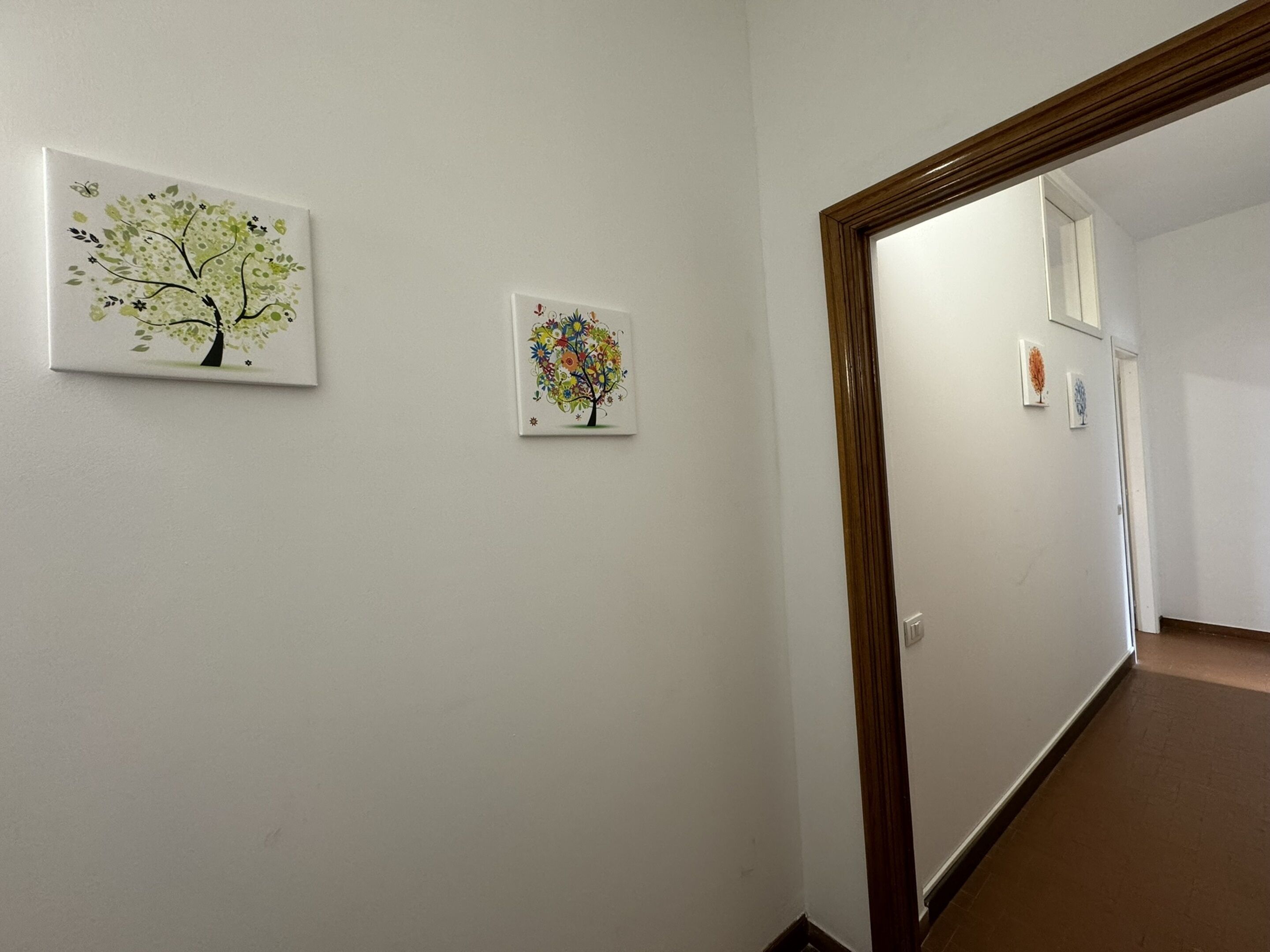 Un pasillo con dos cuadros enmarcados en la pared, un marco de puerta de madera y un espejo que refleja parte del pasillo.