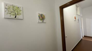Un pasillo con dos cuadros enmarcados en la pared, un marco de puerta de madera y un espejo que refleja parte del pasillo.