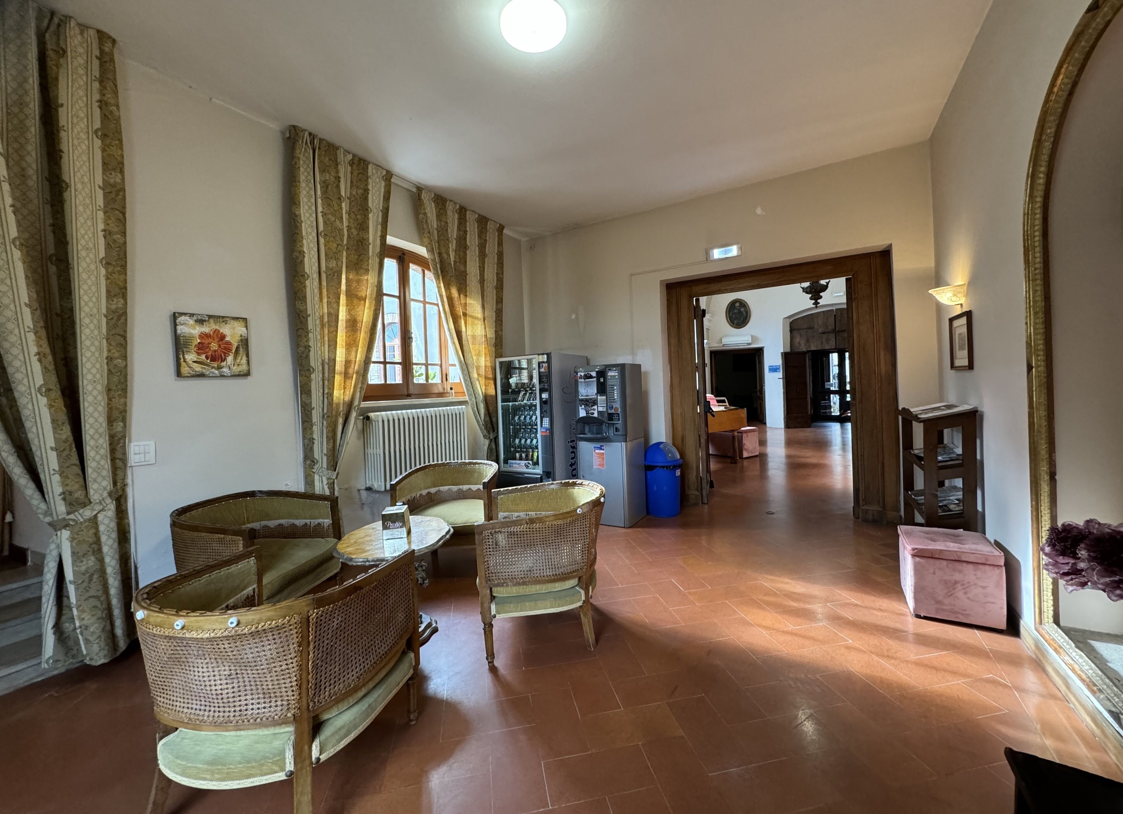 A spacious living area with wicker furniture, a radiator, a vending machine, and a view of the hallway.