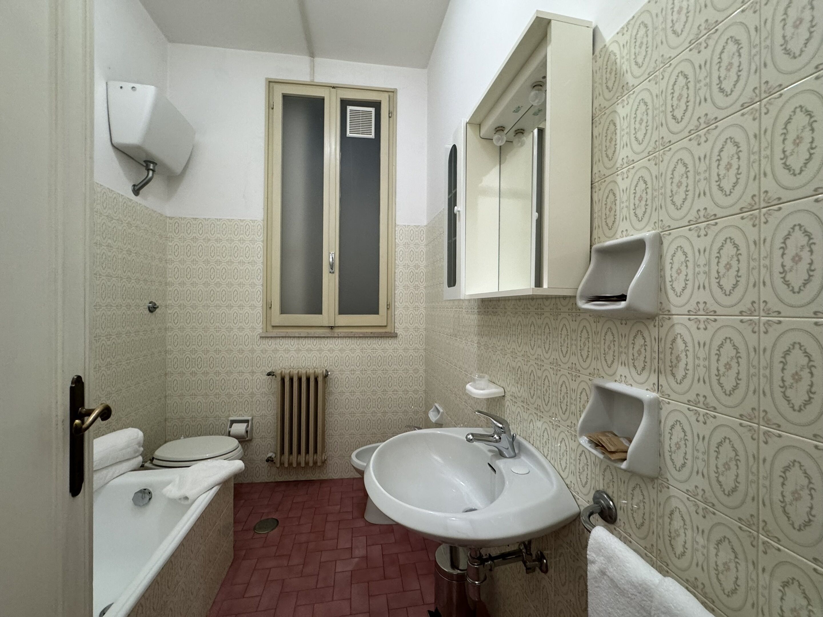 Une petite salle de bain comprenant des toilettes, un lavabo et une fenêtre située au-dessus du radiateur.