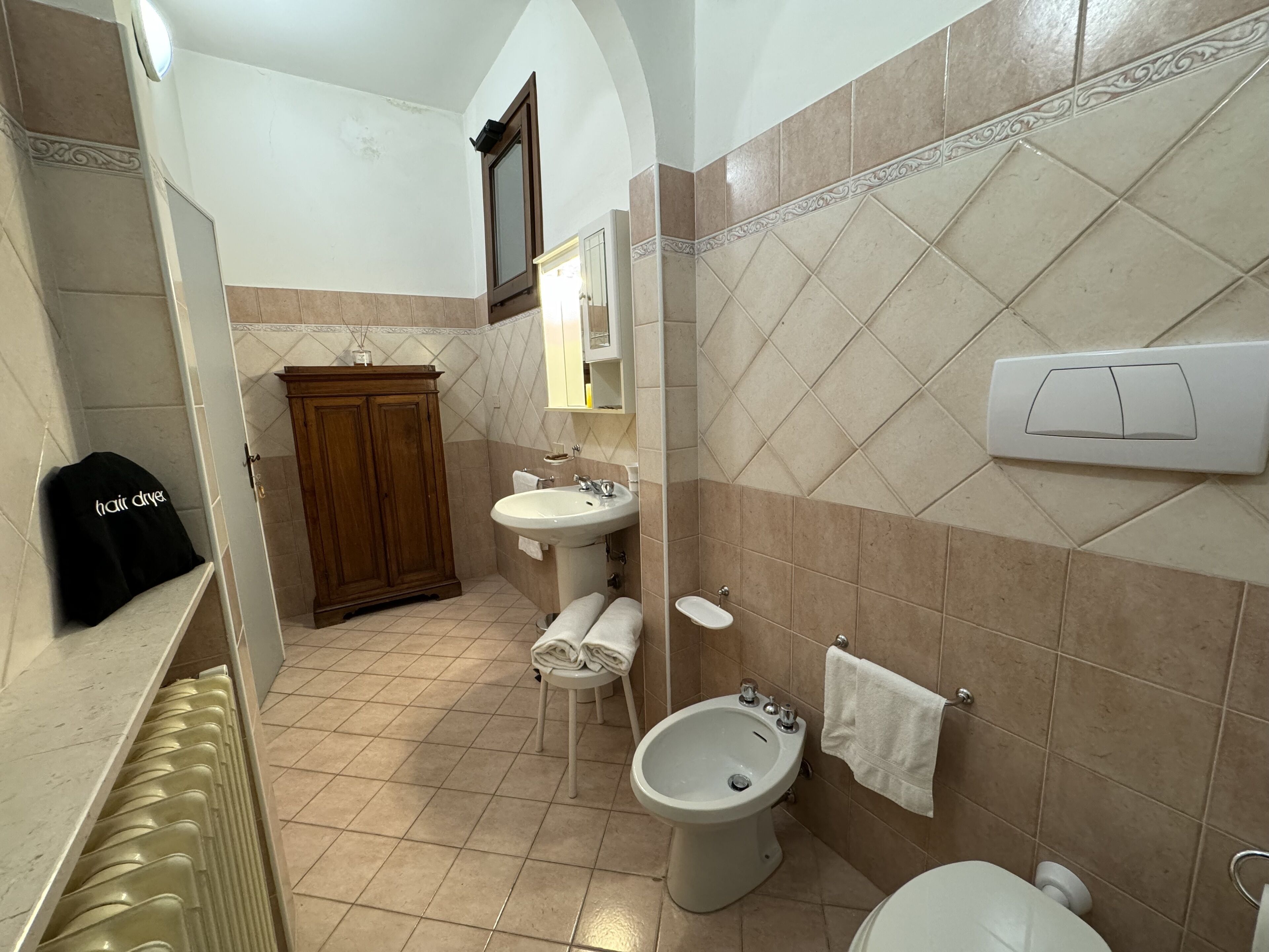 A bathroom with a sink, bidet, and toilet. There is a wooden cabinet and a towel rack.