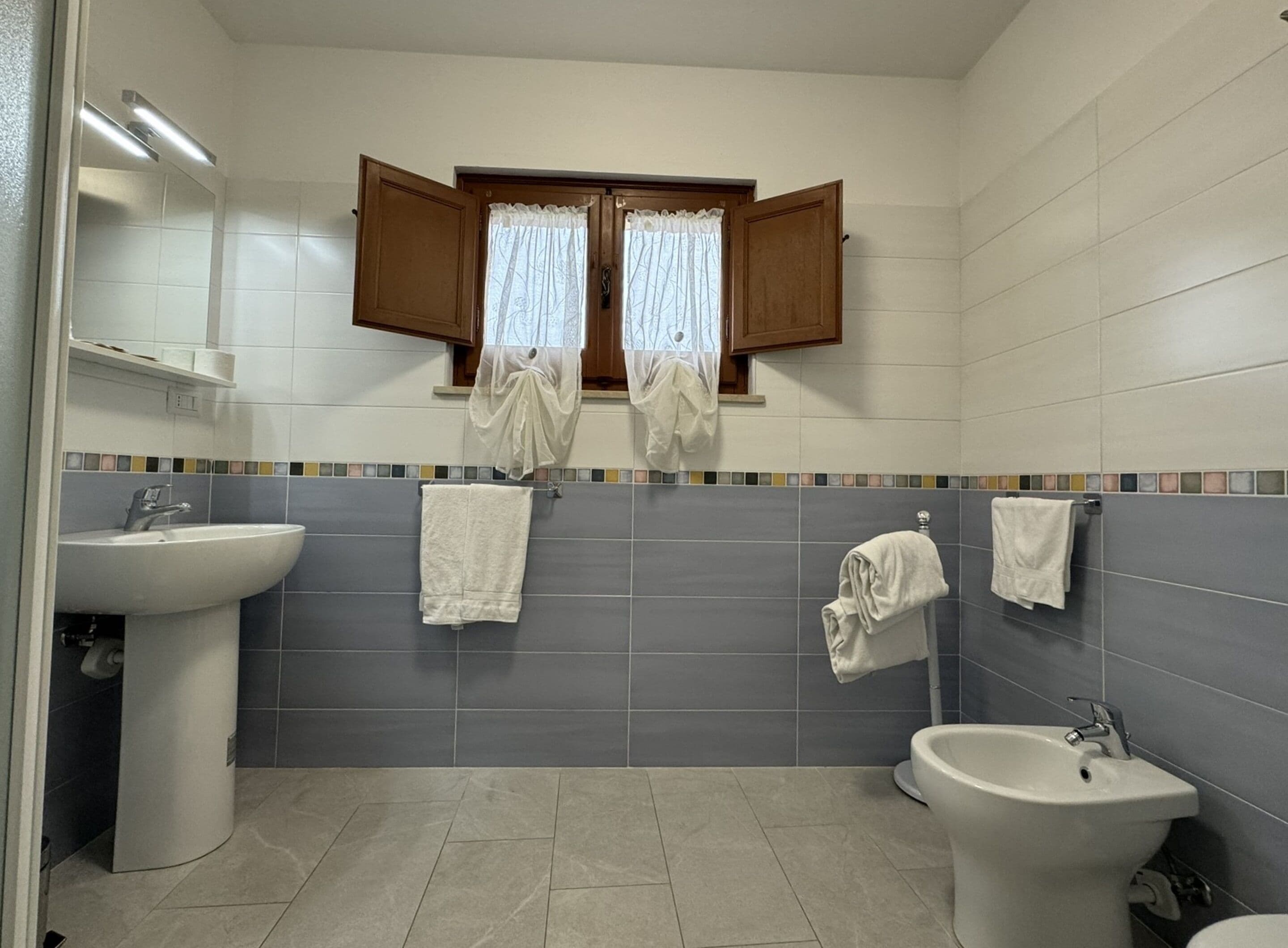 Une salle de bain avec deux lavabos, un bidet et une fenêtre avec des rideaux.