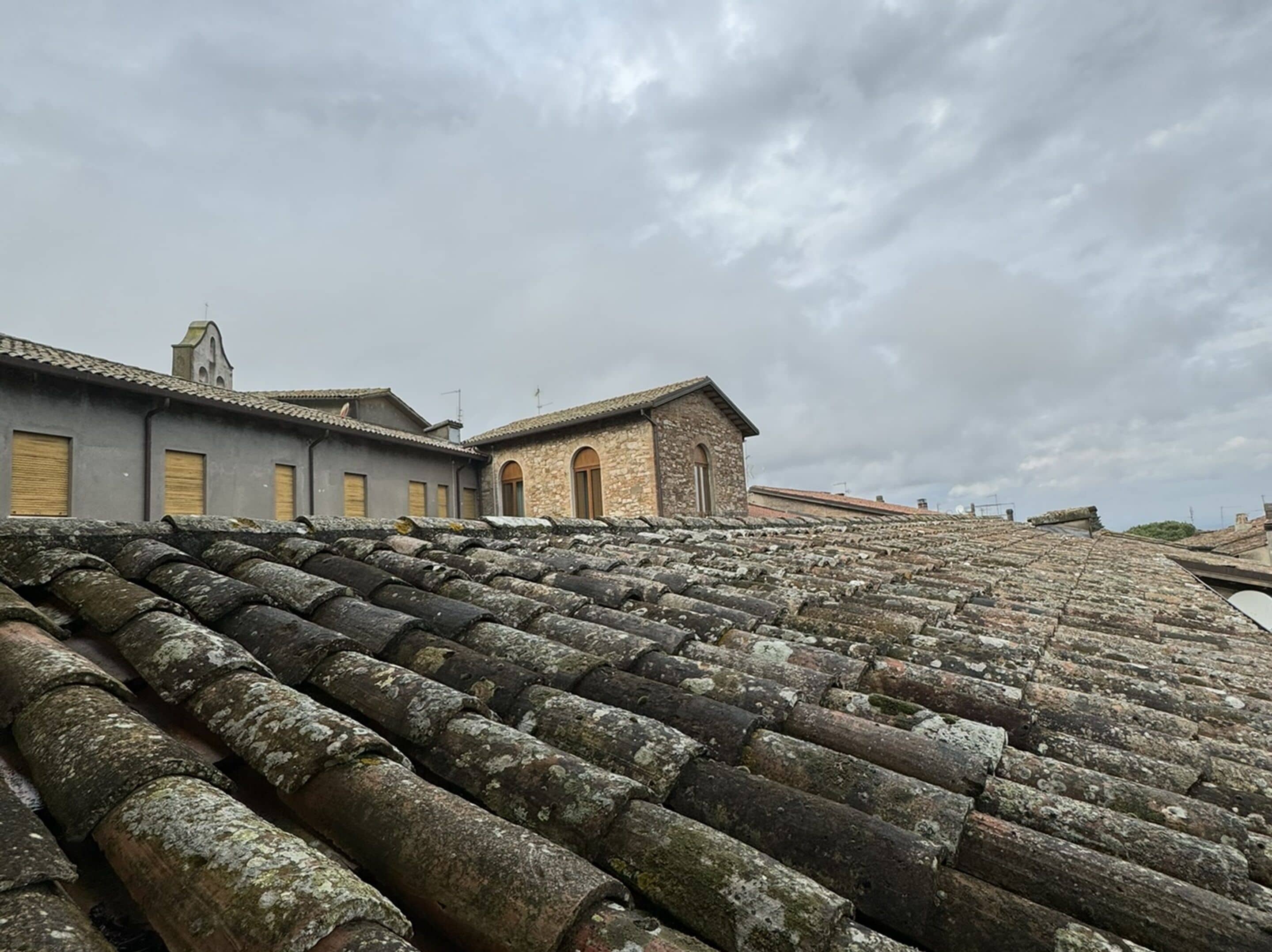 A terraced roof with stone tiles, a building with a stone facade, and a grey building with yellow shutters.