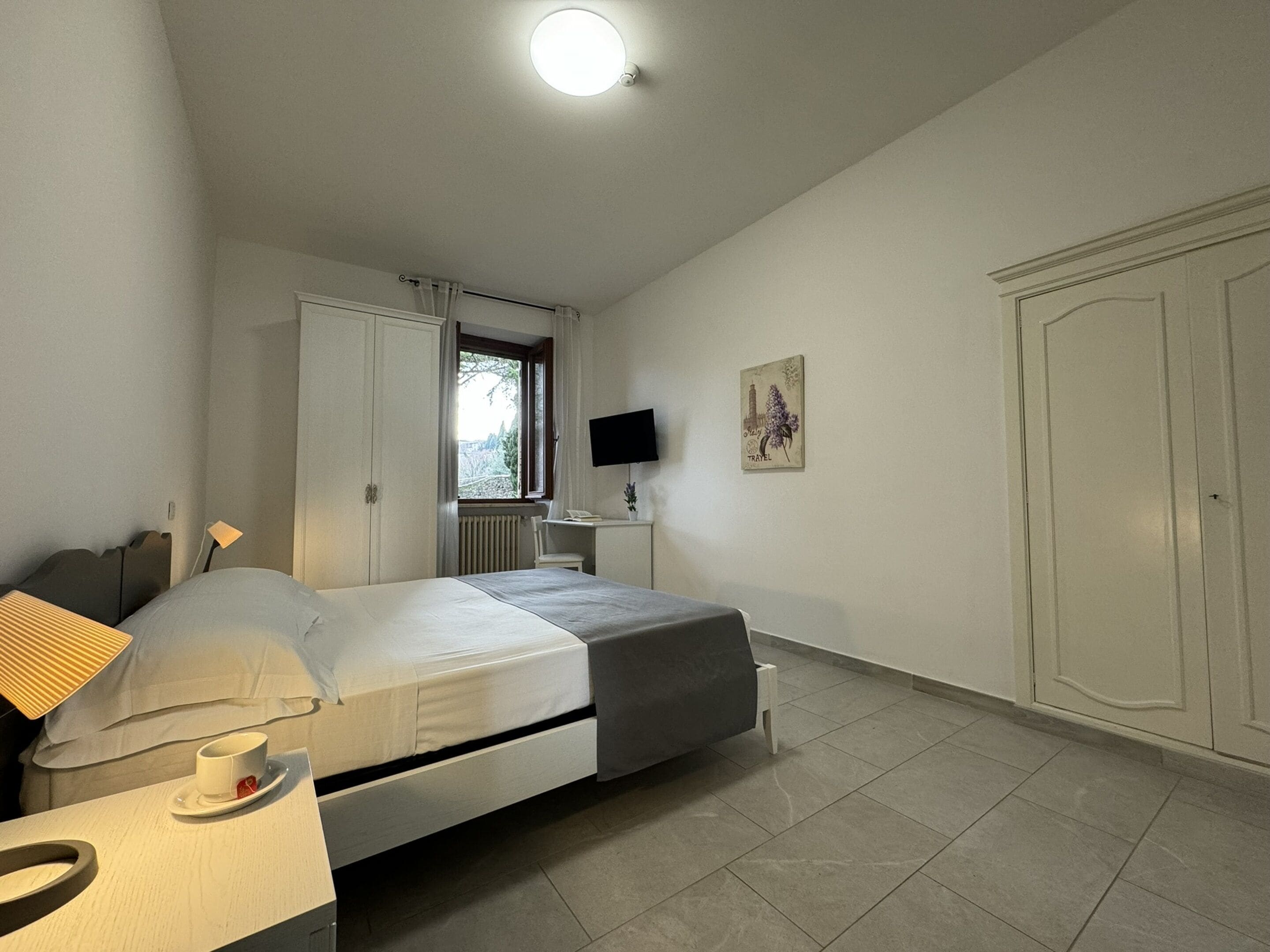 Un dormitorio con cama, mesita de noche, lámpara, televisor y armario.