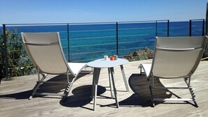 Een terras met twee stoelen en een kleine tafel, met uitzicht op een heldere blauwe oceaan.