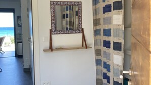 Een kamer met een spiegel aan de muur, een hanglamp en uitzicht op de oceaan door een open deur.