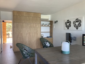 Quarto moderno com guarda-roupa de madeira, mesa de jantar, duas cadeiras, chaleira e prateleiras fixas com objetos decorativos.