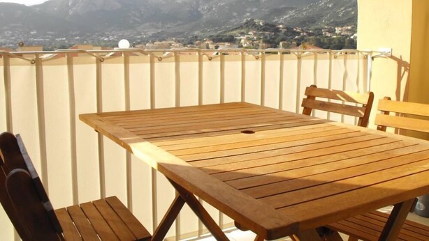 Mesa y sillas de madera en un balcón con vista a la montaña.