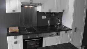 Una cocina moderna con armarios blancos, una encimera negra, una campana extractora de acero inoxidable, un horno integrado y un fregadero.