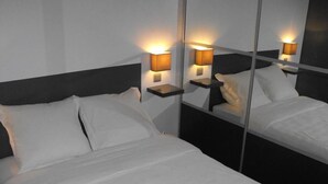 Una cama bien hecha con sábanas blancas y un cabecero, flanqueada por dos mesitas de noche con lámparas.