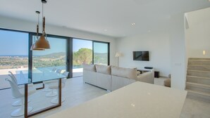 Un salon moderne avec une table à manger en verre, des canapés blancs et une grande fenêtre offrant une vue panoramique.