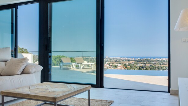 Un salon moderne avec un canapé, une table basse et une vue sur le paysage urbain, visible à travers de grandes portes vitrées.