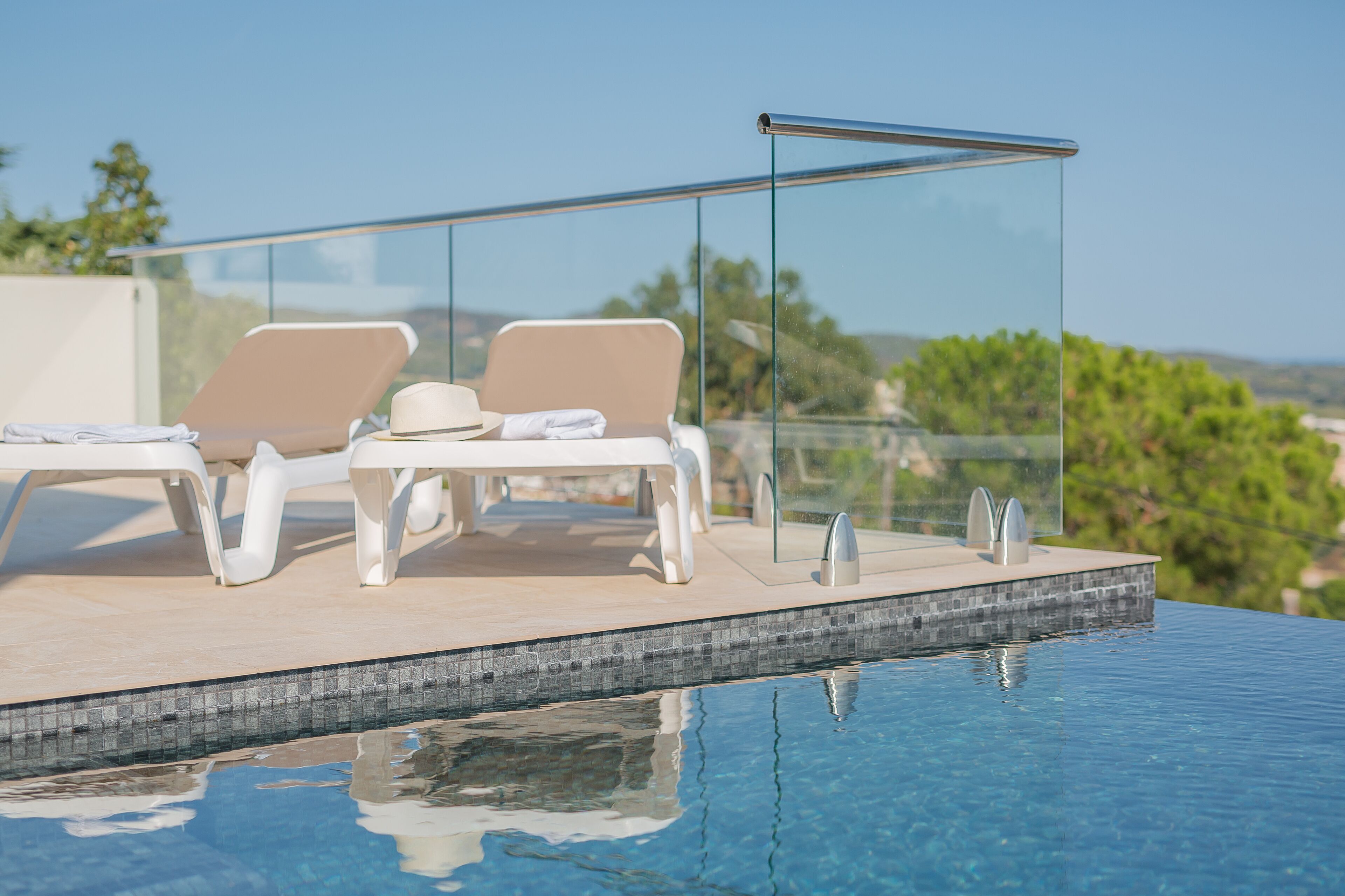 Un espace aménagé au bord de la piscine, avec des chaises longues et une balustrade en verre donnant sur un paysage.
