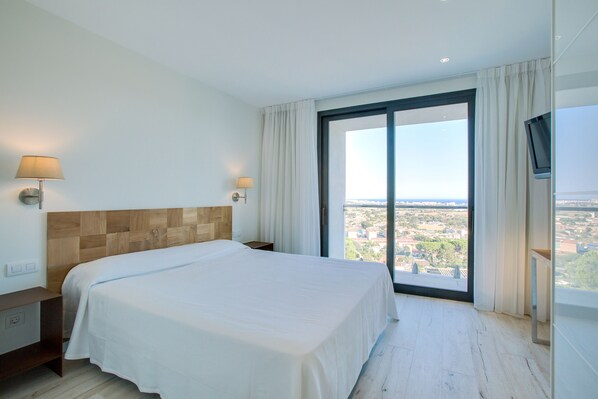 Una habitación de hotel con una cama grande, una mesita de noche, una lámpara y un televisor.