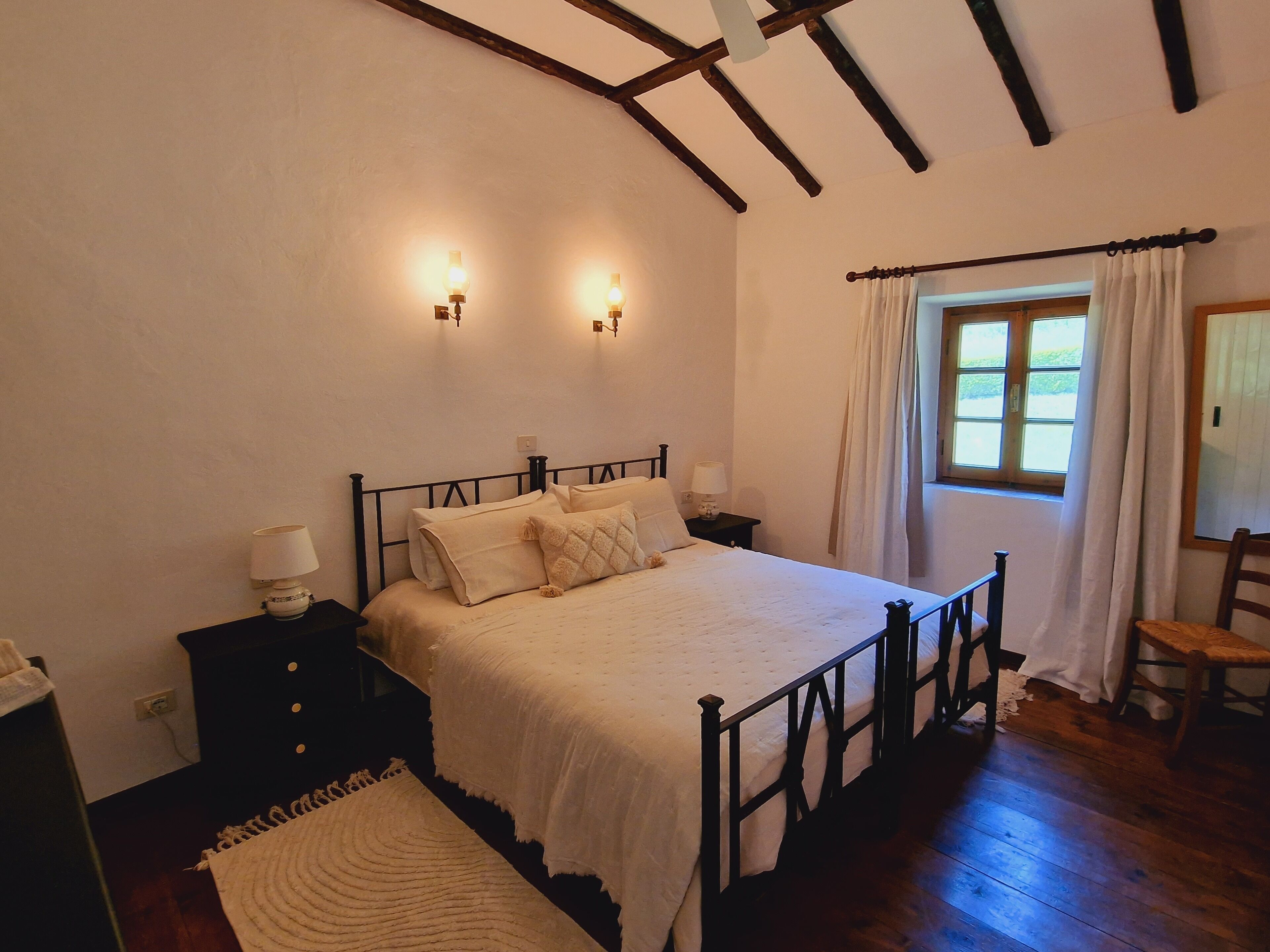 A bedroom with a bed, bedside tables, a window with curtains, and a wooden floor.