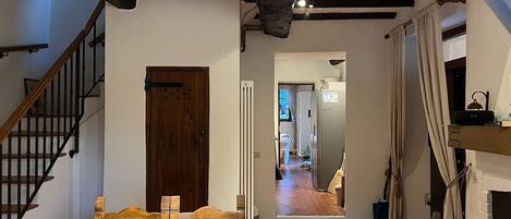 A rustic room with exposed wooden beams, a wooden door, a staircase, and a view into a kitchen area.
