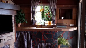 A kitchen with a tiled backsplash, a window with curtains, and various potted plants. - Very cozy stone house (Breña Alta)