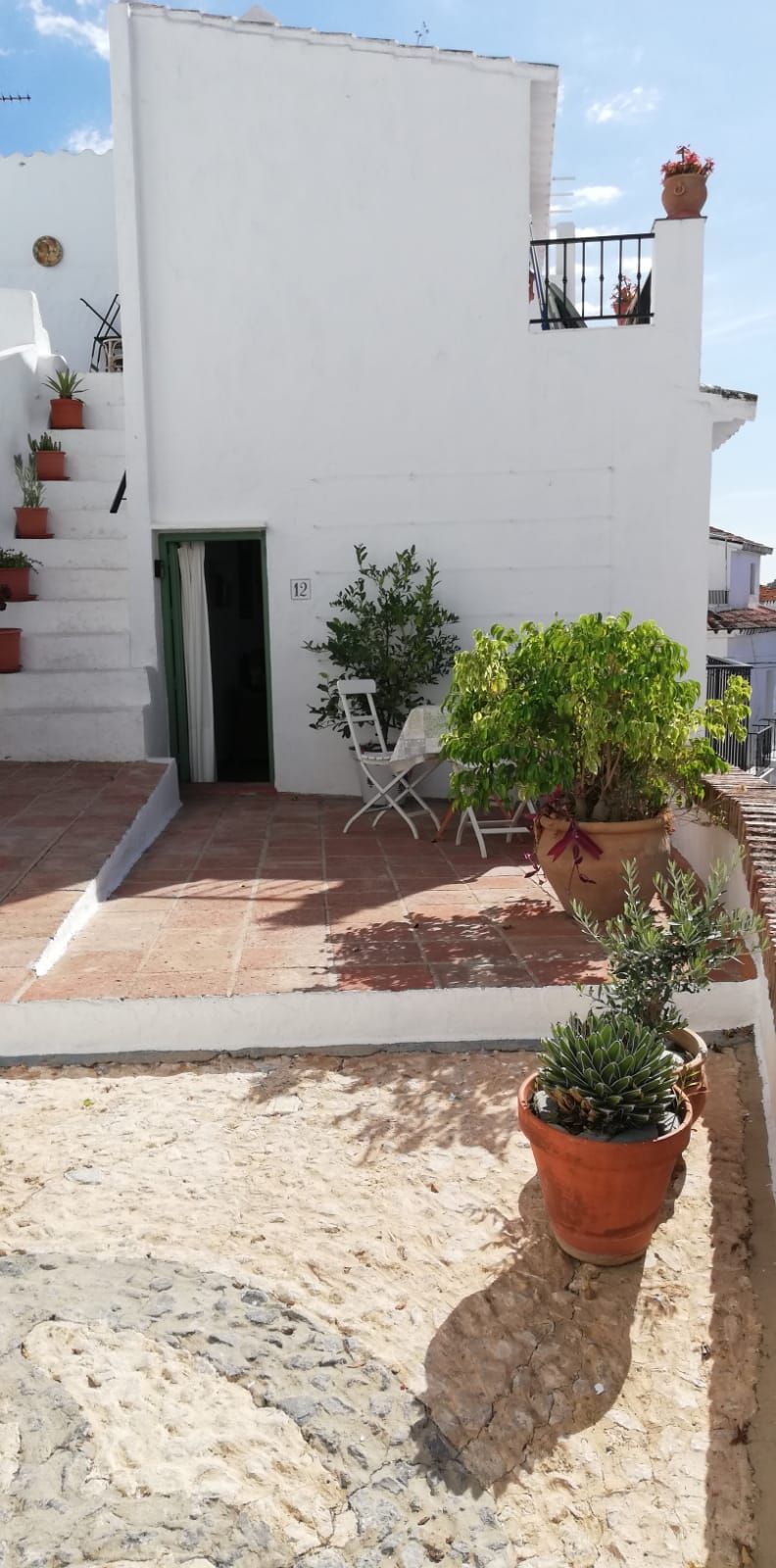 Ein weißes Gebäude mit einer gefliesten Terrasse, Blumentöpfen und einem weißen Stuhl.