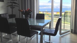 A dining area with a table, chairs, a potted plant, and a view of the sea through large windows. - Luxury  Repouso do Milhafre 181/AL (Horta)