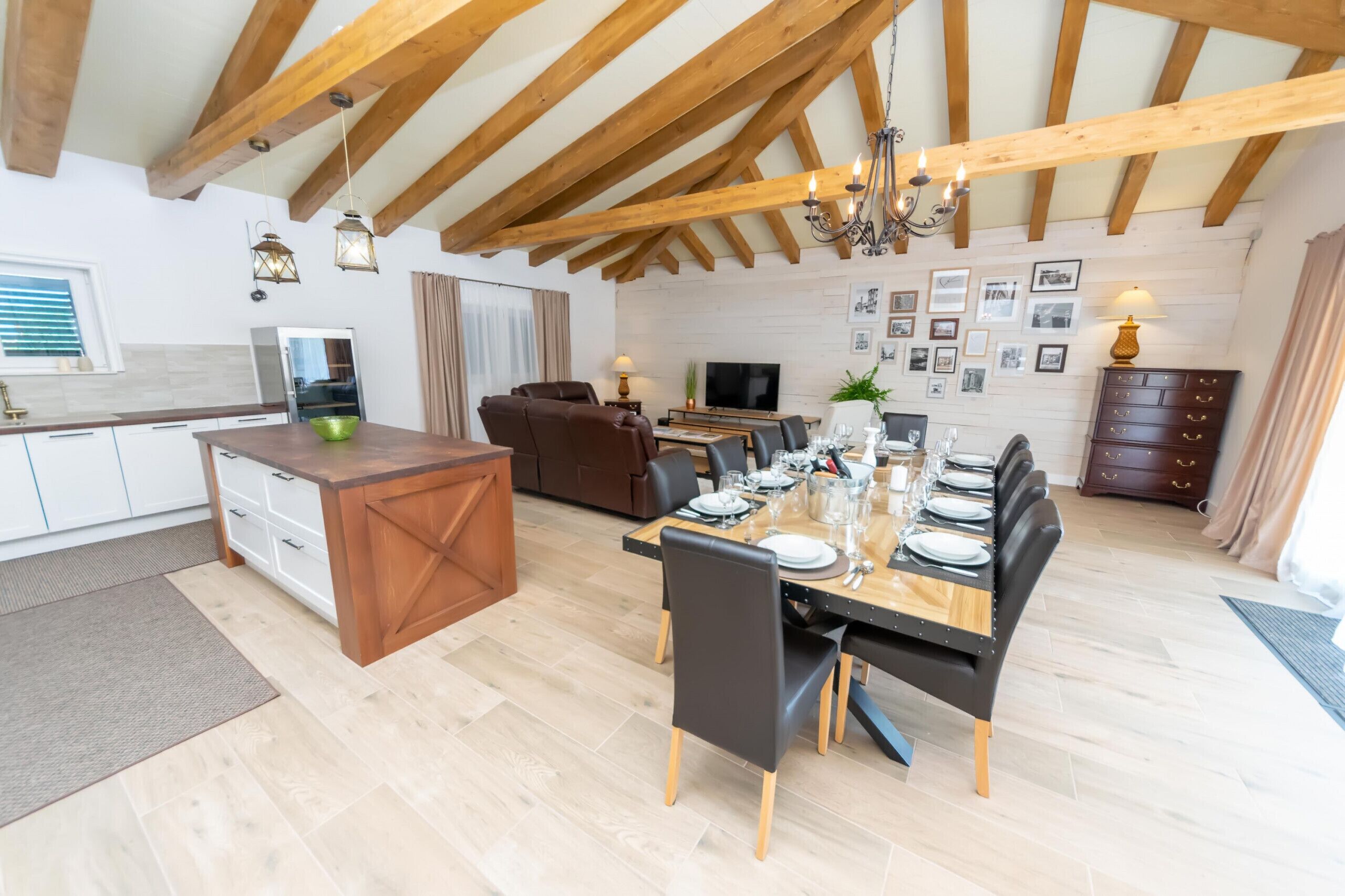 A spacious living area with a dining table set for six, a kitchen with modern appliances, and a loft-style ceiling with exposed beams.