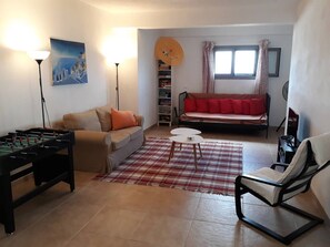 A living room with a foosball table, a sofa, a chair, a coffee table, and a red and white checkered rug. - A modern villa in a unique setting with stunning views. The real Greece. (Metamorfosi)