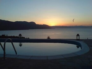 A swimming pool with a view of the sunset over a body of water, surrounded by mountains. - A modern villa in a unique setting with stunning views. The real Greece. (Metamorfosi)